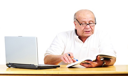 An elderly man working on some paers and his laptop